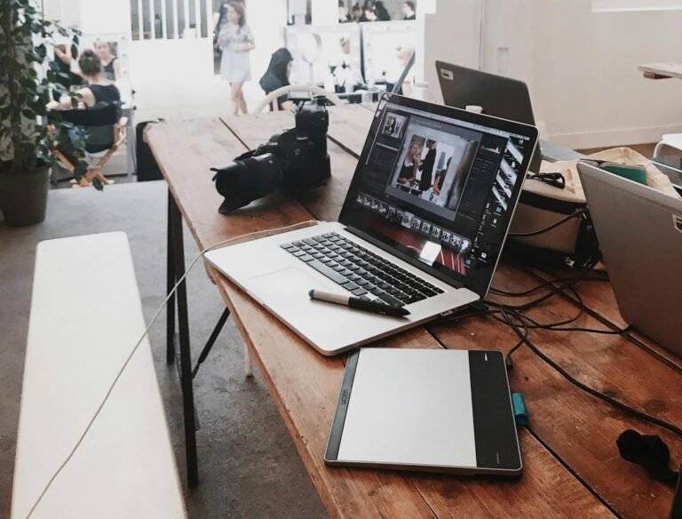 A bright, modern workspace featuring laptops, a camera, and a drawing tablet in an indoor office.