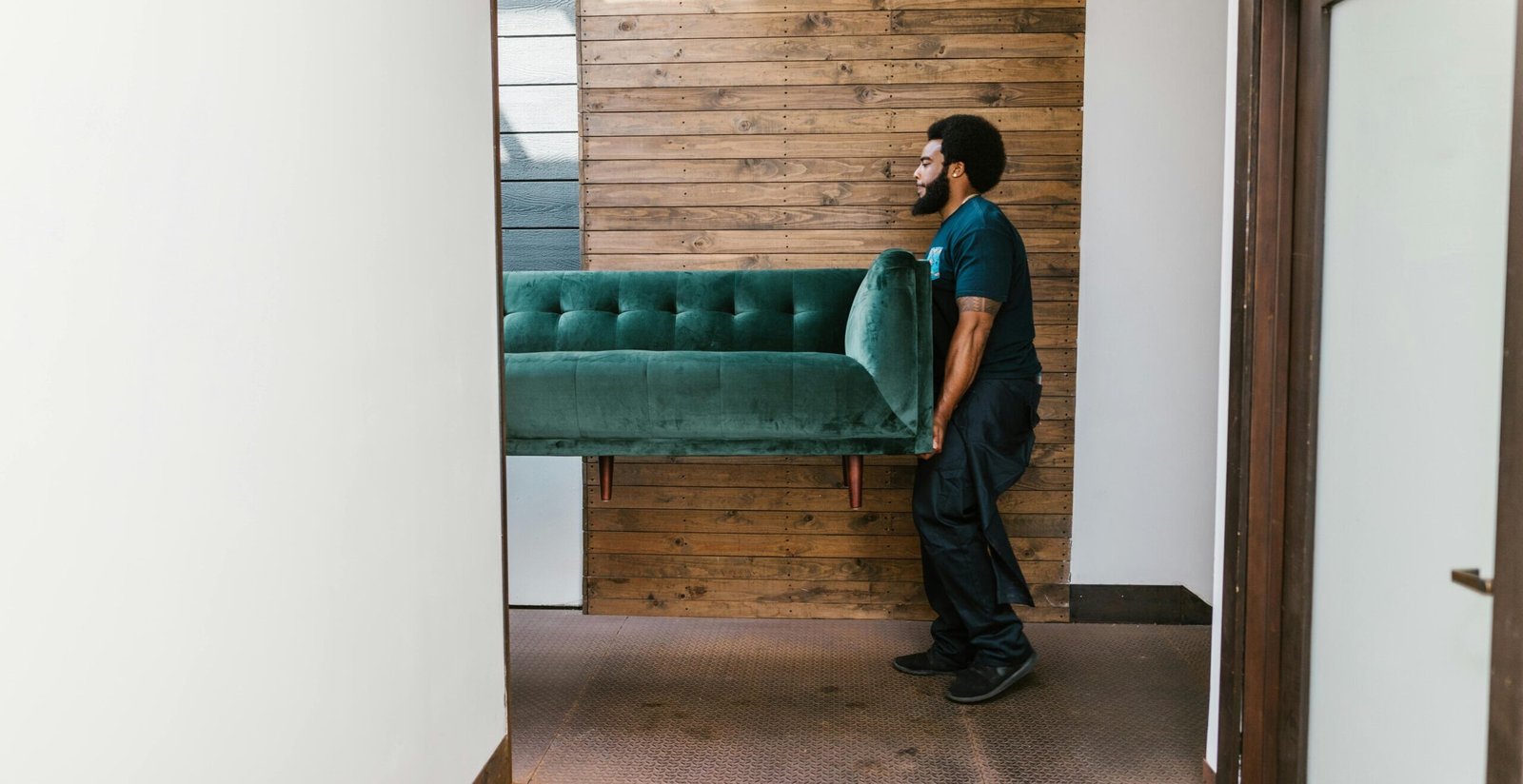 A mover carries a green sofa indoors, showcasing modern interior design and relocation services.