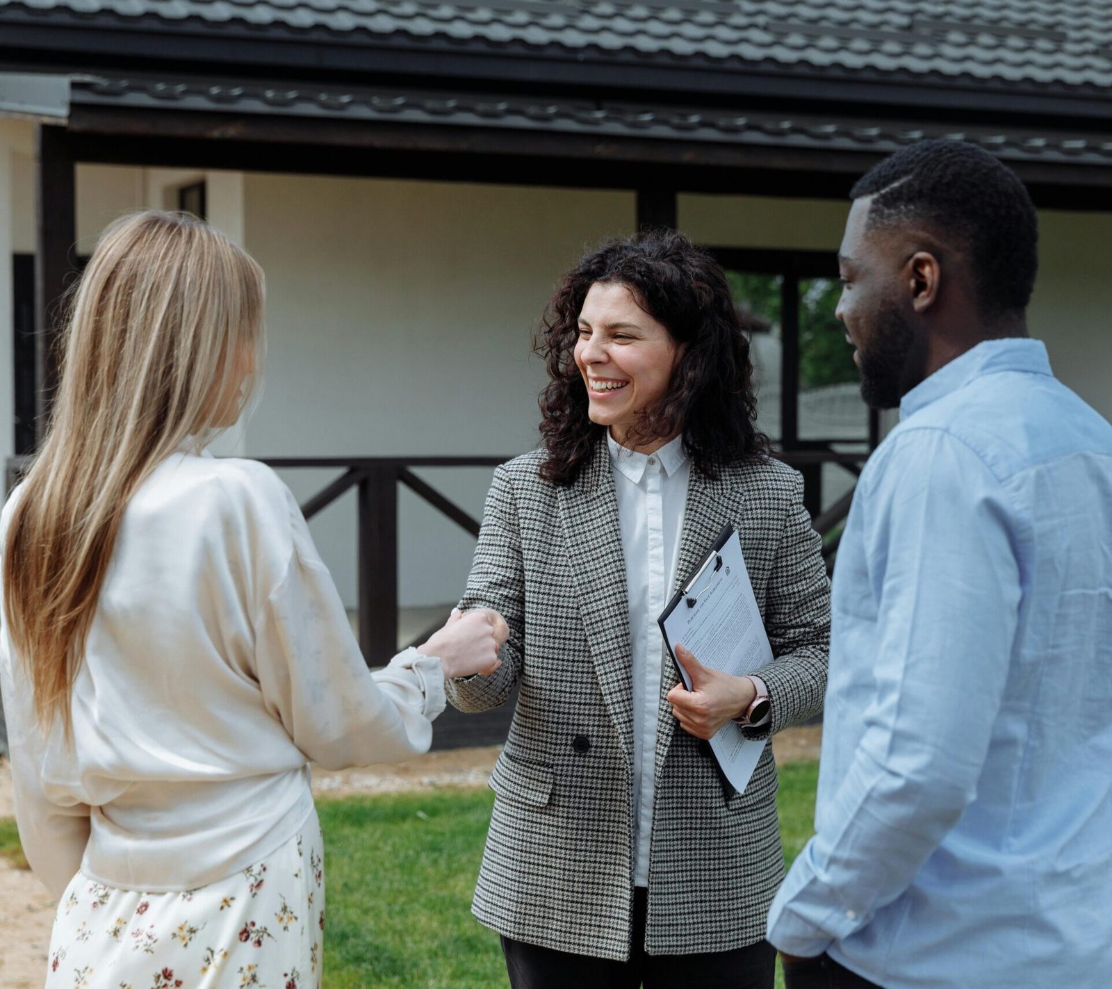 A real estate agent shakes hands with a couple outside a modern house, symbolizing a successful property deal.